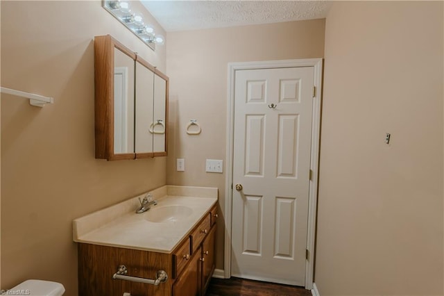 half bath with toilet, a textured ceiling, and vanity