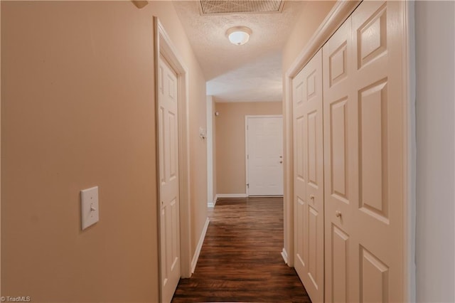 hallway with dark wood-style flooring, visible vents, a textured ceiling, and baseboards