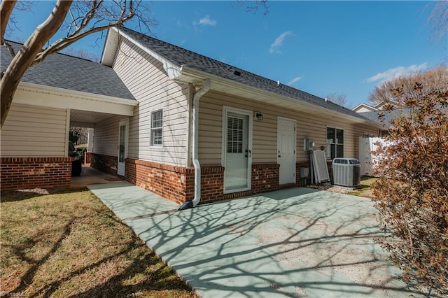 back of property featuring a patio area, brick siding, roof with shingles, and central AC unit