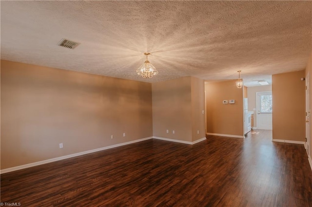 spare room with dark wood-type flooring, visible vents, baseboards, and an inviting chandelier