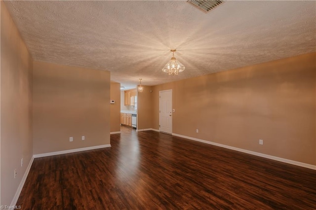 empty room with a notable chandelier, visible vents, dark wood-type flooring, a textured ceiling, and baseboards