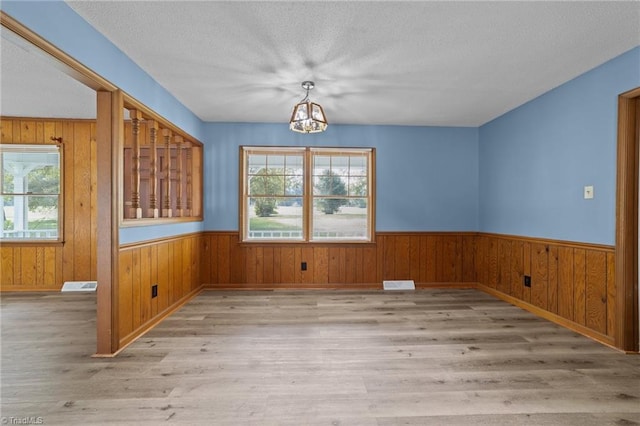 unfurnished dining area featuring a notable chandelier, wooden walls, light hardwood / wood-style floors, and a textured ceiling