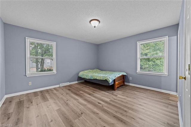 unfurnished bedroom with multiple windows, a textured ceiling, and light hardwood / wood-style floors