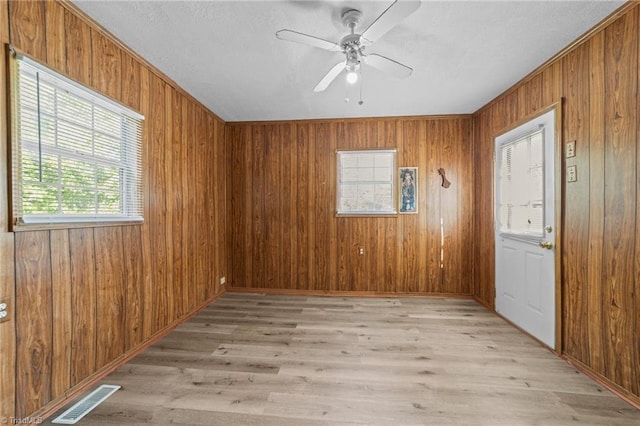 spare room featuring light wood-type flooring, wood walls, and plenty of natural light