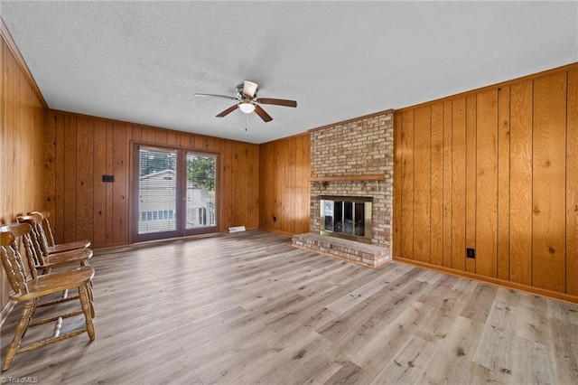 unfurnished living room with a textured ceiling, wood walls, light hardwood / wood-style flooring, a brick fireplace, and ceiling fan