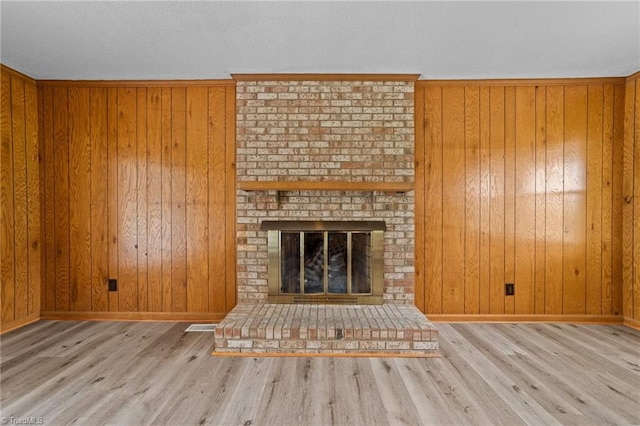 unfurnished living room featuring light wood-type flooring, a fireplace, and wooden walls