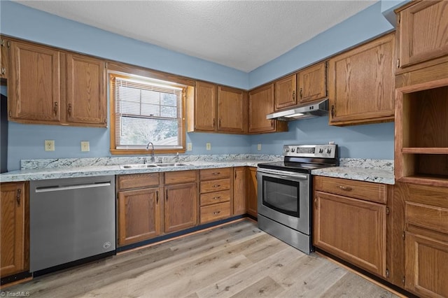 kitchen with light stone countertops, light hardwood / wood-style floors, appliances with stainless steel finishes, and sink