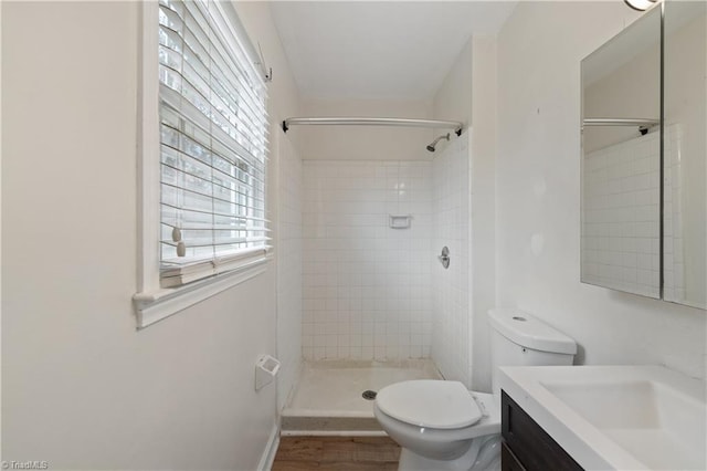 bathroom featuring vanity, toilet, wood finished floors, and a tile shower