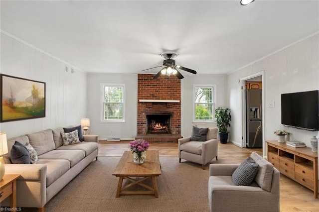 living room featuring crown molding, a brick fireplace, a ceiling fan, and light wood-type flooring