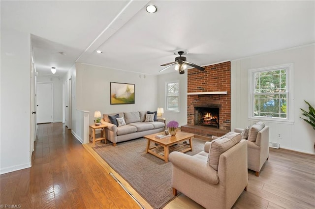 living room with a ceiling fan, visible vents, baseboards, light wood-style floors, and a brick fireplace