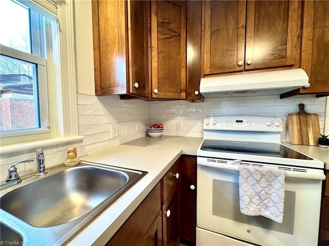 kitchen featuring white range with electric stovetop, tasteful backsplash, light countertops, a sink, and under cabinet range hood