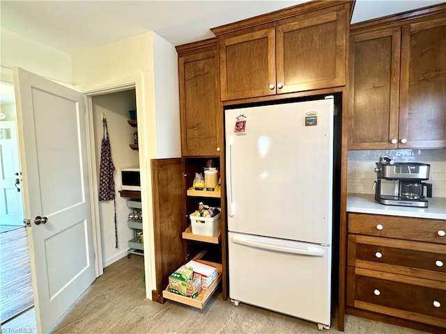 kitchen featuring decorative backsplash, brown cabinets, light countertops, and freestanding refrigerator