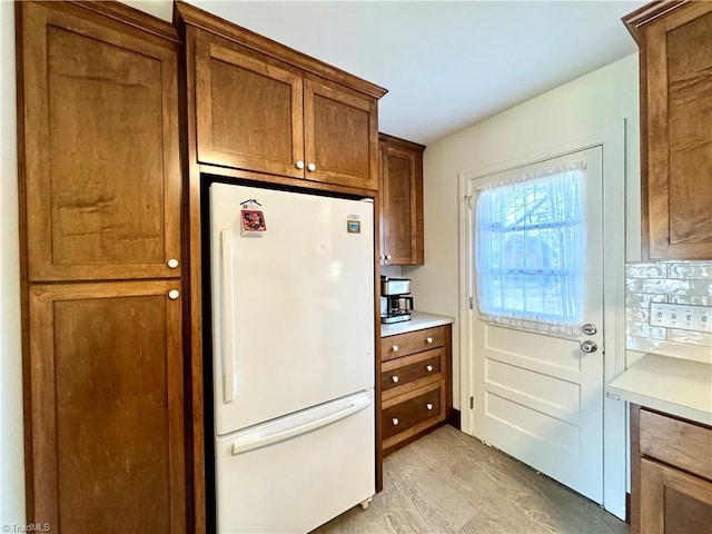 kitchen featuring brown cabinets, light countertops, decorative backsplash, and freestanding refrigerator