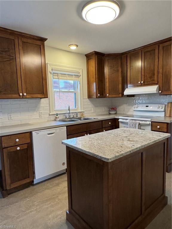 kitchen featuring white appliances, a sink, light stone countertops, under cabinet range hood, and backsplash