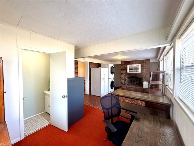 office with stacked washer and dryer, brick wall, a brick fireplace, and a textured ceiling