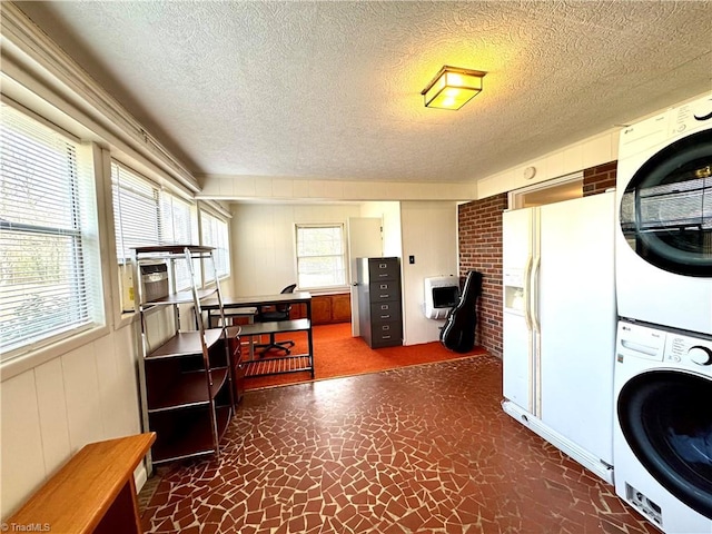 clothes washing area featuring a textured ceiling, stacked washer and dryer, wood walls, and laundry area