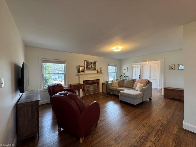 living room featuring a brick fireplace, dark wood-style flooring, and baseboards