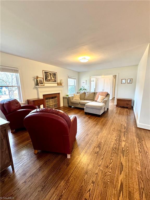 living room featuring a brick fireplace, wood finished floors, and a healthy amount of sunlight