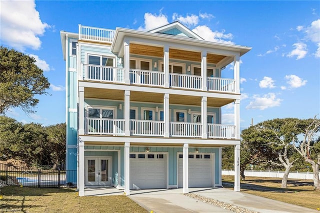 beach home with an attached garage, fence, concrete driveway, french doors, and a balcony
