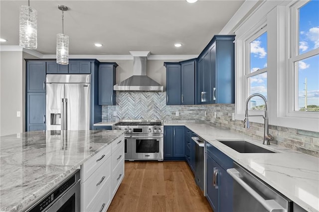 kitchen with wall chimney exhaust hood, blue cabinetry, light stone counters, a sink, and built in appliances