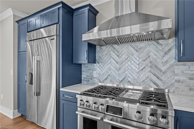 kitchen featuring wall chimney exhaust hood, light wood-type flooring, blue cabinets, premium appliances, and decorative backsplash