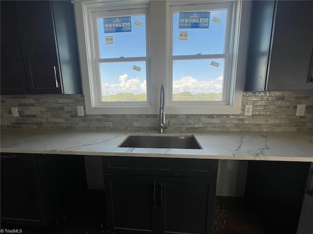 kitchen with decorative backsplash, light stone countertops, and sink