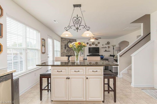 kitchen with a breakfast bar area, ceiling fan, dark stone counters, and decorative light fixtures