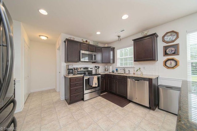kitchen with appliances with stainless steel finishes, a sink, dark brown cabinets, tasteful backsplash, and recessed lighting