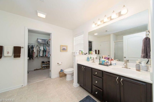 full bath featuring a stall shower, double vanity, toilet, a walk in closet, and baseboards