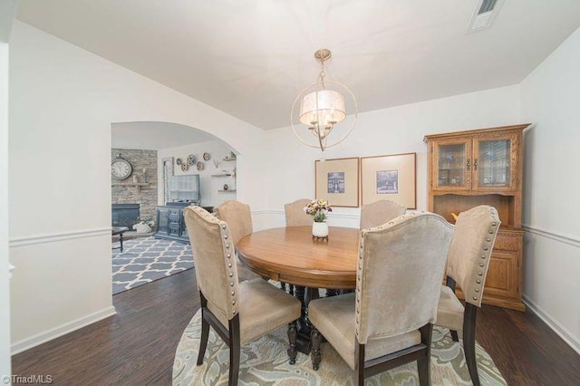 dining room featuring dark wood-type flooring, a chandelier, baseboards, and arched walkways