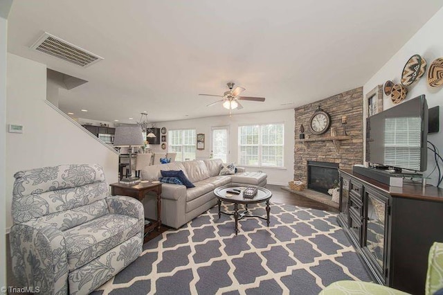 living area with a stone fireplace, ceiling fan, and wood finished floors
