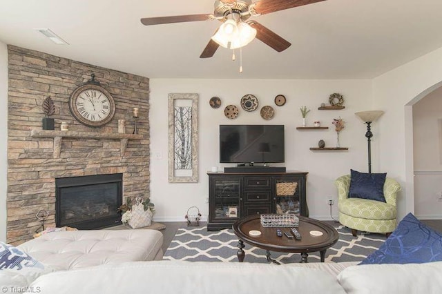 living area featuring arched walkways, ceiling fan, baseboards, and a fireplace