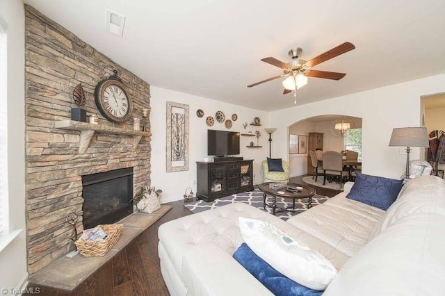 living room with arched walkways, a stone fireplace, wood finished floors, and ceiling fan