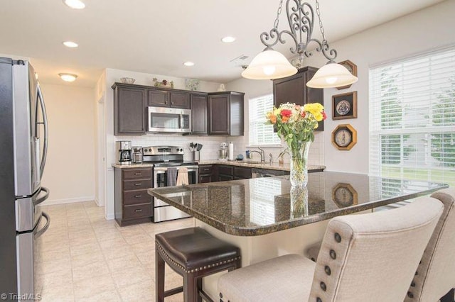 kitchen with appliances with stainless steel finishes, dark brown cabinets, a kitchen bar, recessed lighting, and tasteful backsplash