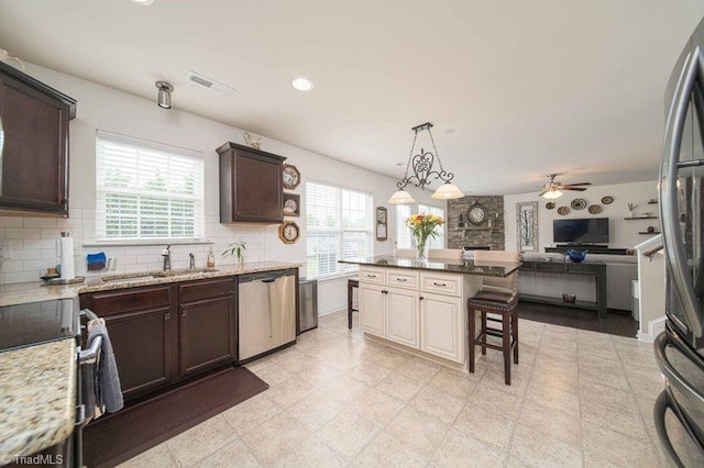 kitchen with appliances with stainless steel finishes, a sink, open floor plan, dark brown cabinets, and a kitchen breakfast bar