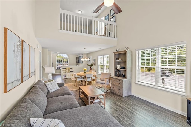 living room with baseboards, wood finished floors, ceiling fan with notable chandelier, and a high ceiling