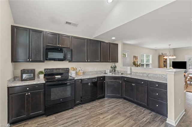 kitchen featuring lofted ceiling, a sink, a peninsula, black appliances, and light wood-style floors