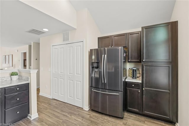 kitchen with light wood-type flooring, stainless steel fridge, dark brown cabinets, and visible vents