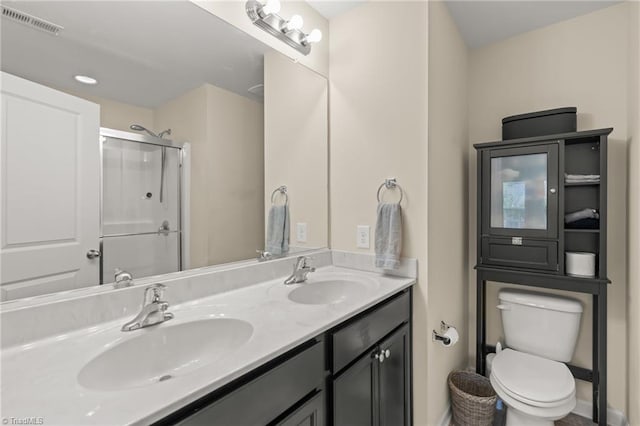 full bathroom with toilet, a shower with shower door, double vanity, and a sink