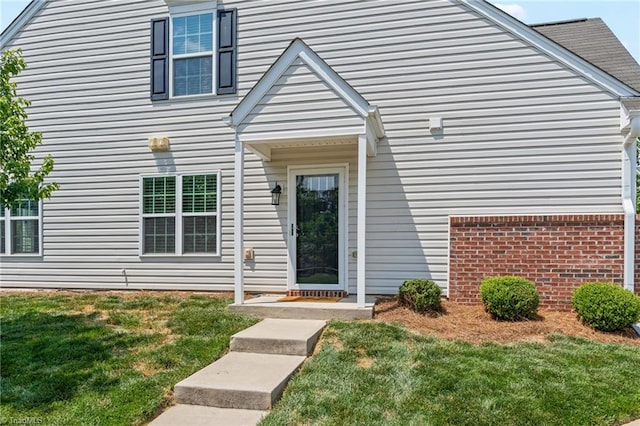 entrance to property with brick siding and a lawn