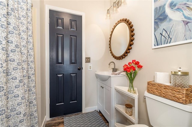 bathroom with toilet, wood finished floors, vanity, baseboards, and curtained shower