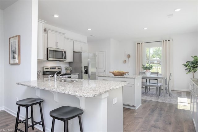 kitchen featuring a kitchen bar, appliances with stainless steel finishes, a sink, a peninsula, and recessed lighting