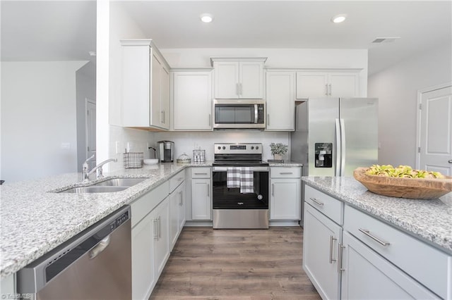 kitchen featuring light stone counters, a sink, stainless steel appliances, white cabinetry, and dark wood-style floors