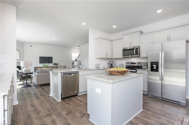kitchen with light stone countertops, dark wood finished floors, stainless steel appliances, open floor plan, and white cabinetry