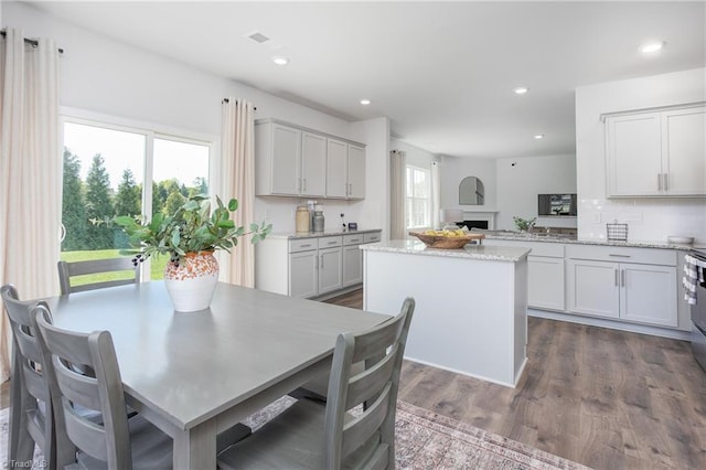 kitchen with light stone countertops, a center island, recessed lighting, tasteful backsplash, and dark wood-type flooring