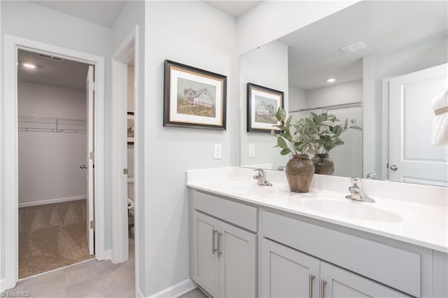 bathroom featuring double vanity, a sink, baseboards, and a spacious closet