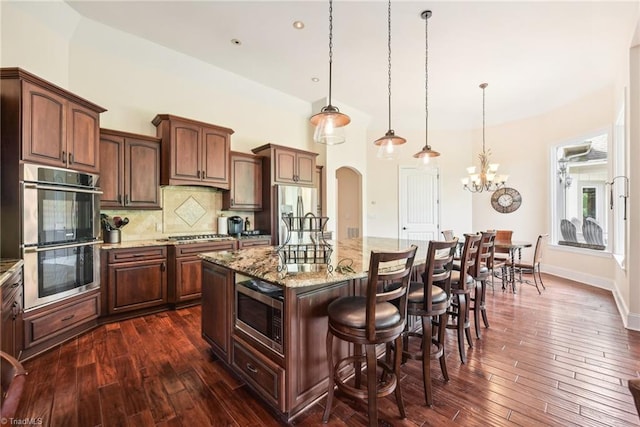 kitchen with decorative light fixtures, appliances with stainless steel finishes, a chandelier, an island with sink, and dark wood-type flooring