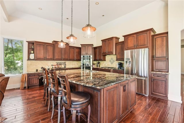 kitchen with a spacious island, pendant lighting, backsplash, appliances with stainless steel finishes, and dark wood-type flooring