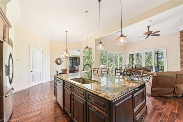 kitchen with ceiling fan with notable chandelier, a center island with sink, appliances with stainless steel finishes, dark wood-type flooring, and sink