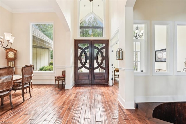 foyer with ornamental molding, light hardwood / wood-style flooring, a high ceiling, and an inviting chandelier